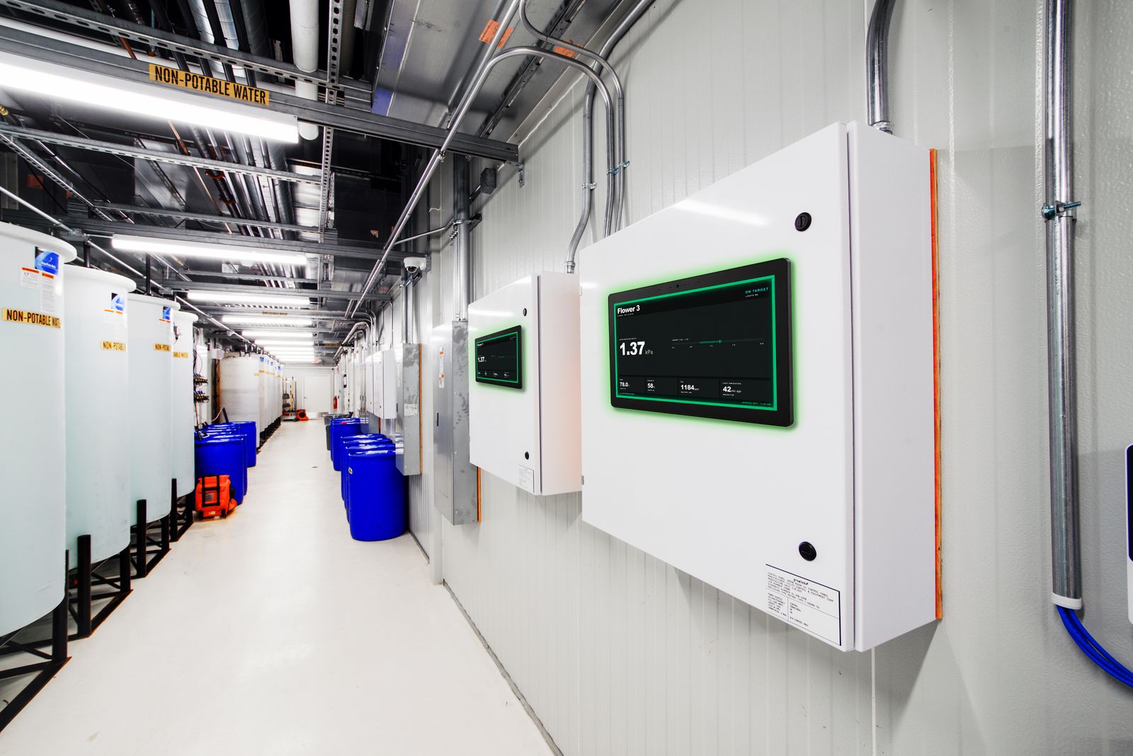 Growlink Core controllers and displayLINK room dashboards installed on facility wall showing live climate data